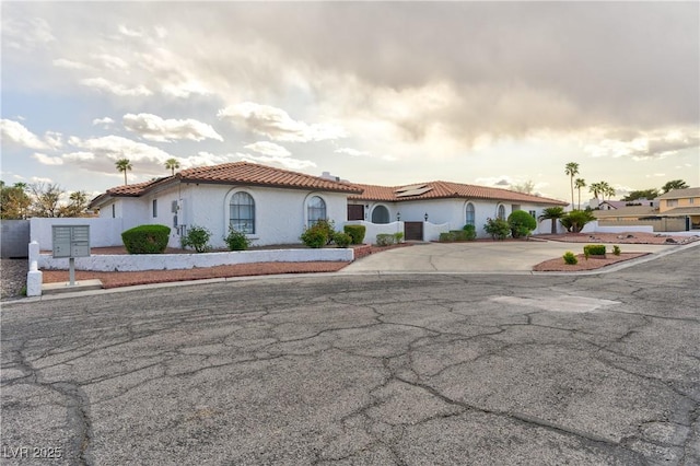 mediterranean / spanish home featuring solar panels, a tile roof, stucco siding, and driveway