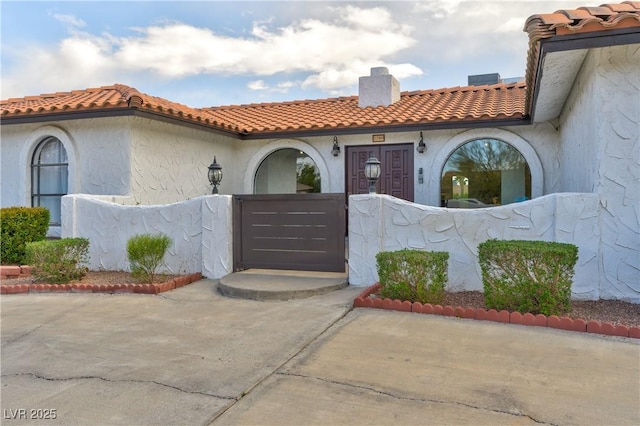 view of exterior entry featuring fence, a tile roof, a chimney, and stucco siding