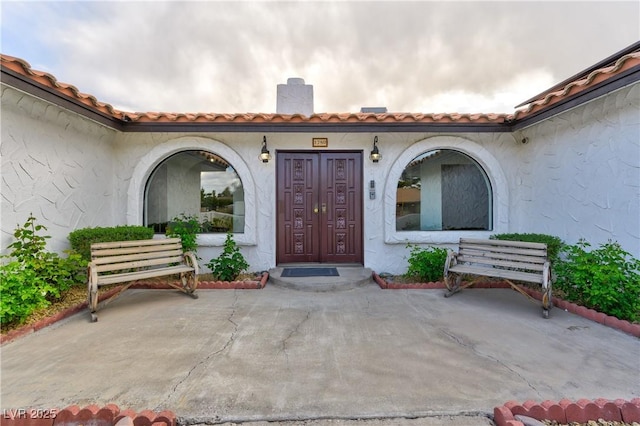 entrance to property featuring a chimney, a tile roof, and stucco siding