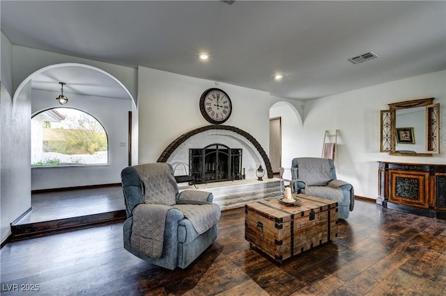 living area with arched walkways, visible vents, hardwood / wood-style floors, and a fireplace with raised hearth