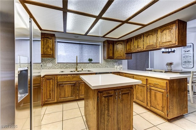 kitchen with a center island, a sink, stainless steel fridge with ice dispenser, light countertops, and a peninsula