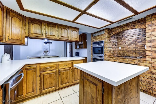 kitchen with light tile patterned flooring, brick wall, light countertops, appliances with stainless steel finishes, and visible vents
