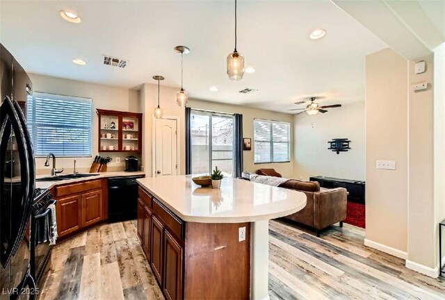 kitchen featuring sink, light hardwood / wood-style flooring, hanging light fixtures, a kitchen island, and black appliances