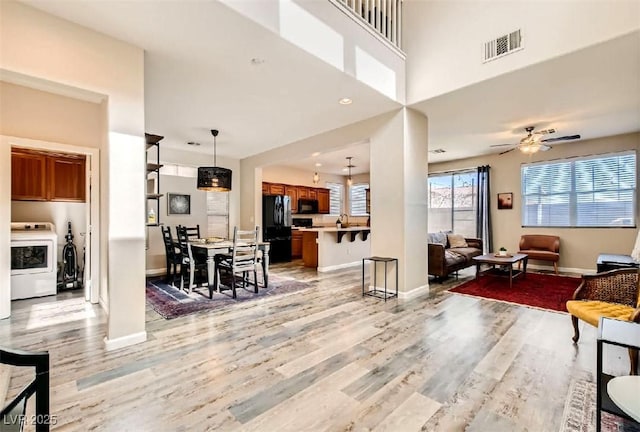 living room featuring sink, light hardwood / wood-style flooring, a towering ceiling, ceiling fan, and washer / clothes dryer