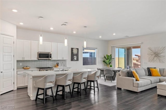 kitchen with tasteful backsplash, stainless steel microwave, a kitchen island with sink, light countertops, and range