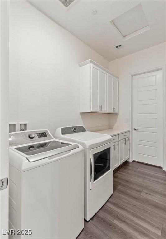 washroom featuring wood finished floors, visible vents, attic access, cabinet space, and washer and clothes dryer