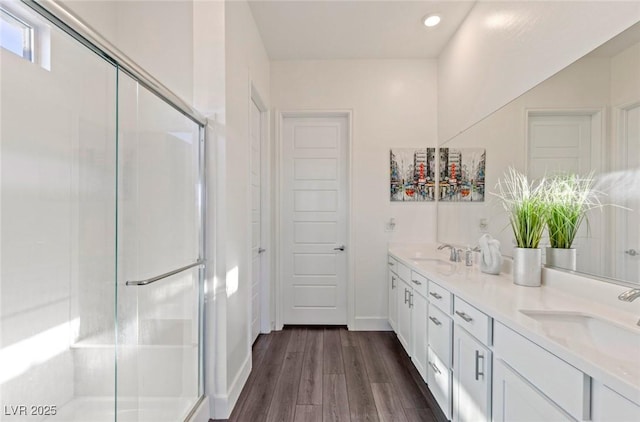 bathroom featuring double vanity, wood finished floors, a stall shower, and a sink