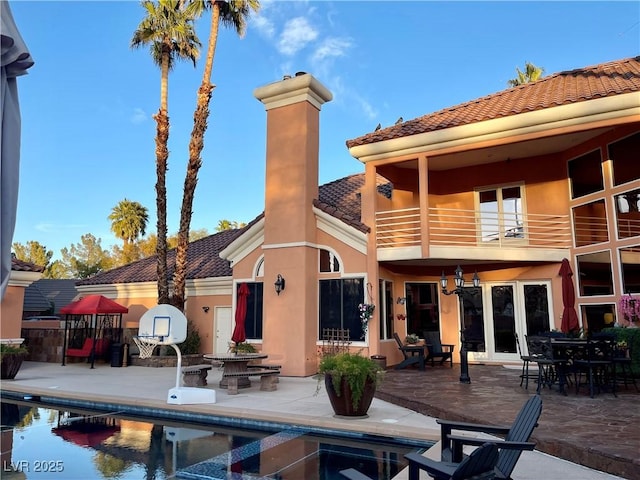 rear view of house with an outdoor pool, a balcony, a tile roof, a patio area, and stucco siding