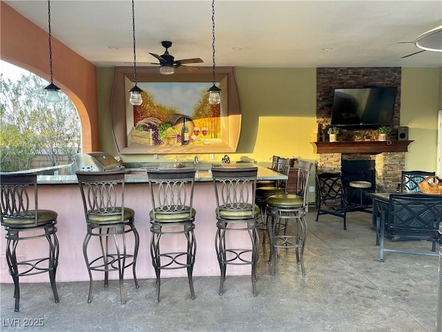 bar with an outdoor stone fireplace, decorative light fixtures, concrete floors, and ceiling fan