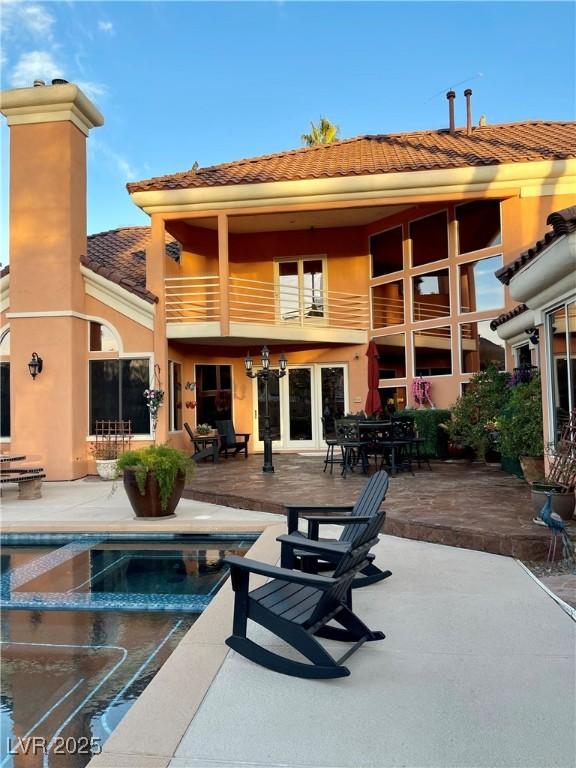 rear view of property with a patio, a balcony, an outdoor pool, a tiled roof, and stucco siding