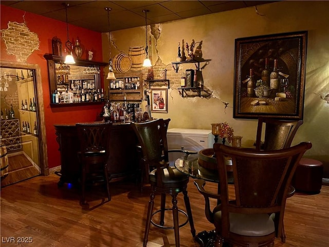 bar with a bar, a drop ceiling, and wood finished floors