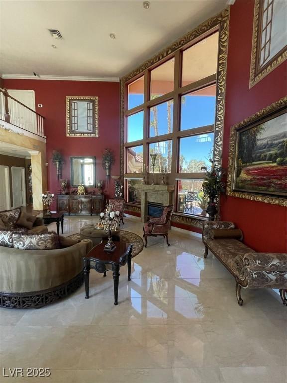 living area with ornamental molding, a glass covered fireplace, a towering ceiling, and visible vents