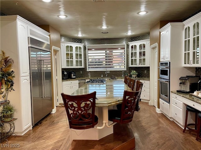 kitchen featuring stainless steel appliances, white cabinetry, glass insert cabinets, and tasteful backsplash