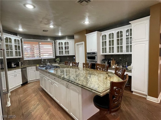 kitchen featuring a center island, a breakfast bar, stainless steel appliances, visible vents, and white cabinets