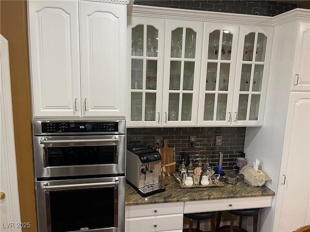 kitchen featuring white cabinetry, glass insert cabinets, backsplash, and stainless steel double oven