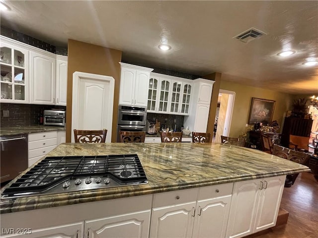 kitchen featuring visible vents, white cabinets, decorative backsplash, glass insert cabinets, and appliances with stainless steel finishes