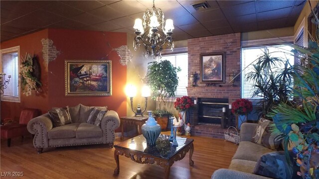 living area with a chandelier, a paneled ceiling, a fireplace, wood finished floors, and visible vents