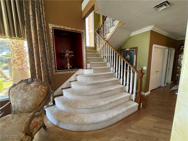 stairway featuring ornamental molding, wood finished floors, visible vents, and baseboards