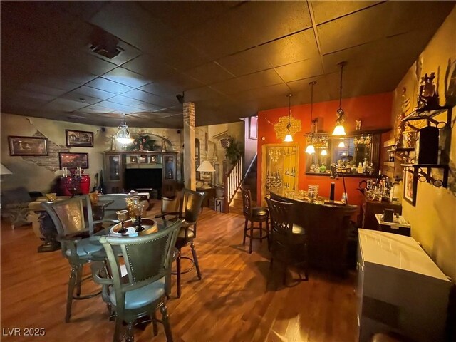 dining area featuring stairs, a bar, wood finished floors, and a paneled ceiling