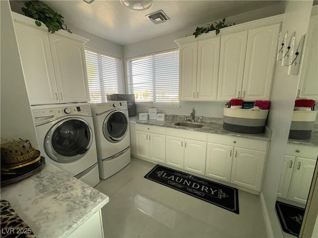 laundry area with a textured ceiling, washing machine and dryer, a sink, visible vents, and cabinet space