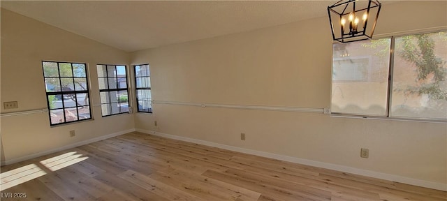 empty room featuring an inviting chandelier, lofted ceiling, and light hardwood / wood-style flooring