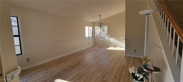 unfurnished dining area with light hardwood / wood-style floors, vaulted ceiling, and a textured ceiling