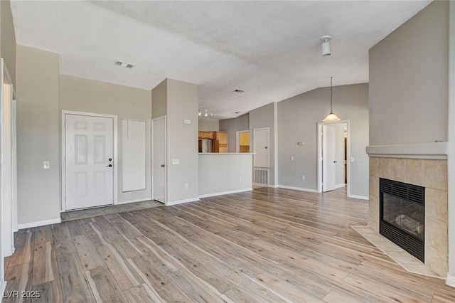 unfurnished living room with lofted ceiling, light hardwood / wood-style floors, and a tile fireplace