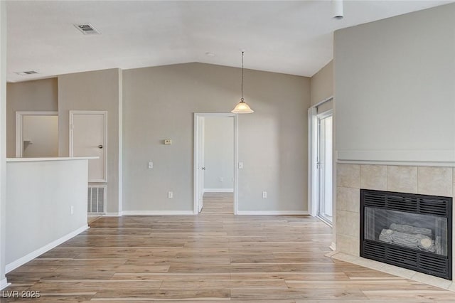 unfurnished living room featuring a tiled fireplace, vaulted ceiling, and light wood-type flooring