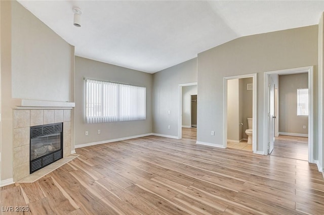 unfurnished living room featuring vaulted ceiling, a tile fireplace, and light hardwood / wood-style floors