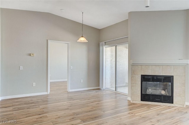 unfurnished living room featuring heating unit, lofted ceiling, a tiled fireplace, and light hardwood / wood-style flooring