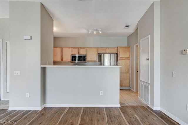 kitchen featuring stainless steel appliances, light brown cabinets, kitchen peninsula, and light hardwood / wood-style flooring