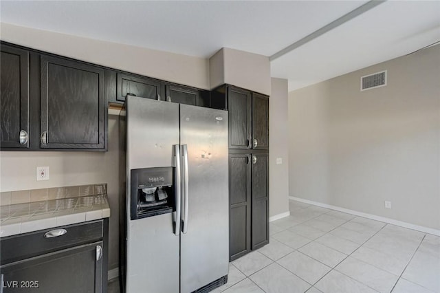 kitchen with stainless steel fridge, tile countertops, dark brown cabinets, and light tile patterned floors