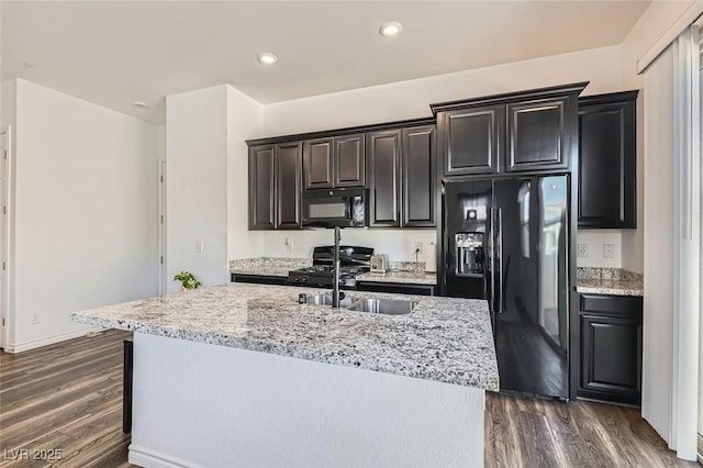 kitchen with sink, light stone counters, a center island with sink, dark hardwood / wood-style floors, and black appliances