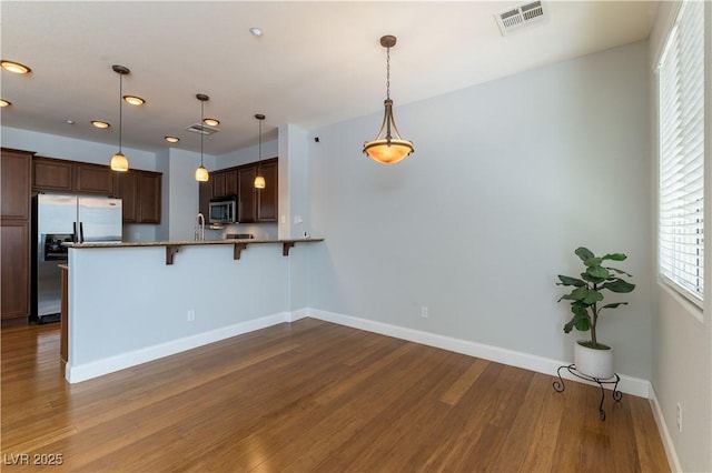 kitchen with a breakfast bar, decorative light fixtures, kitchen peninsula, stainless steel appliances, and light hardwood / wood-style flooring