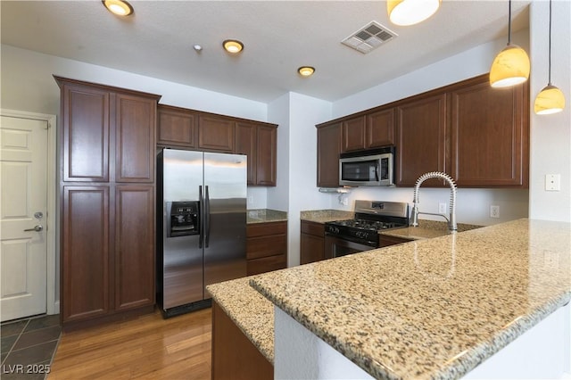 kitchen featuring stainless steel appliances, pendant lighting, light stone counters, and kitchen peninsula