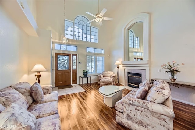 living room featuring a tile fireplace, a towering ceiling, hardwood / wood-style floors, and ceiling fan