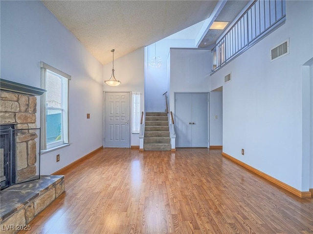 unfurnished living room featuring hardwood / wood-style flooring, a fireplace, high vaulted ceiling, and a textured ceiling