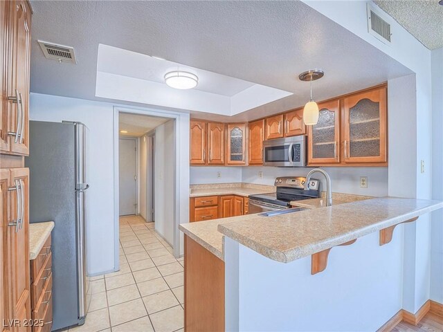 kitchen featuring decorative light fixtures, appliances with stainless steel finishes, a kitchen breakfast bar, kitchen peninsula, and a raised ceiling