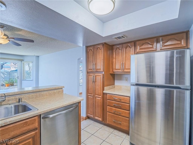 kitchen with appliances with stainless steel finishes, sink, light tile patterned floors, ceiling fan, and a textured ceiling