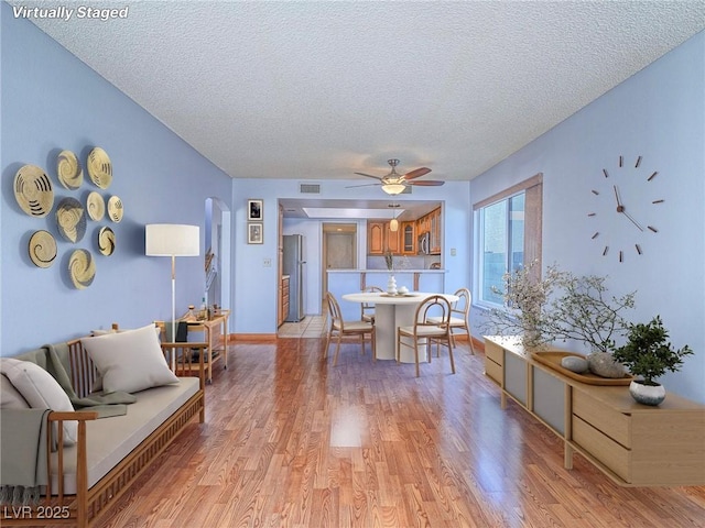 living room with ceiling fan, a textured ceiling, and light wood-type flooring