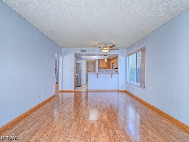 unfurnished living room featuring ceiling fan, a textured ceiling, and light wood-type flooring