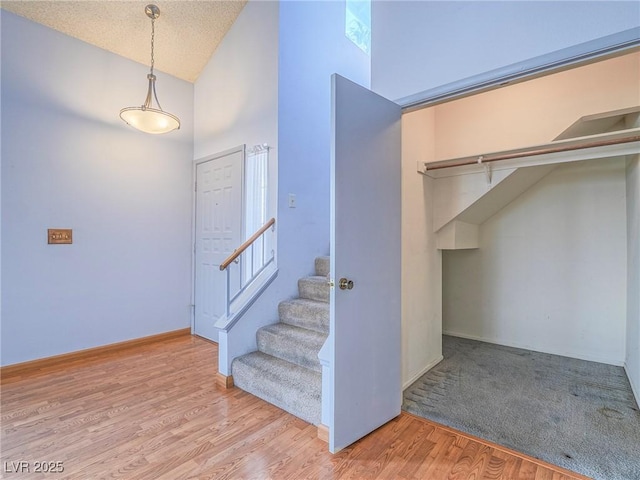 stairs featuring hardwood / wood-style flooring, high vaulted ceiling, and a textured ceiling