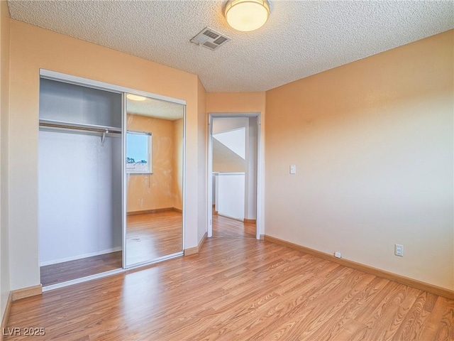 unfurnished bedroom featuring a closet, a textured ceiling, and light hardwood / wood-style flooring