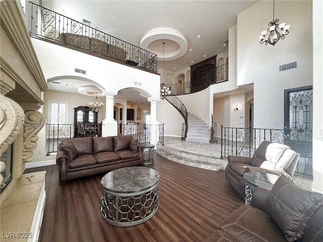 living room with dark hardwood / wood-style flooring, a notable chandelier, decorative columns, and a high ceiling