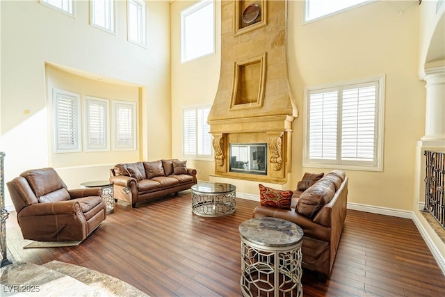 living room featuring a large fireplace, a healthy amount of sunlight, dark hardwood / wood-style floors, and ornate columns