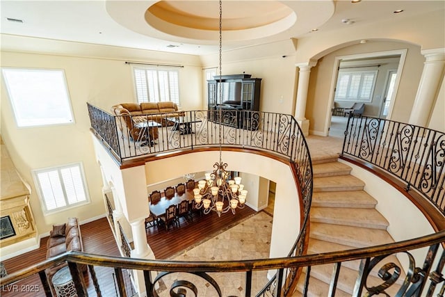 staircase with an inviting chandelier, decorative columns, and a raised ceiling