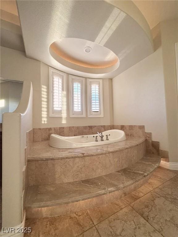 bathroom with a relaxing tiled tub and a raised ceiling