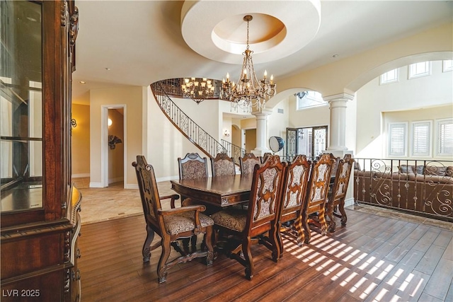 dining room with hardwood / wood-style flooring, a tray ceiling, decorative columns, and a notable chandelier