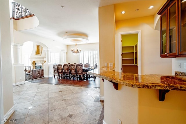 kitchen with dark stone countertops, hanging light fixtures, decorative columns, a kitchen bar, and kitchen peninsula