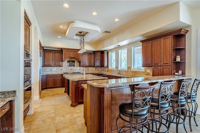 kitchen with sink, light stone counters, a kitchen breakfast bar, kitchen peninsula, and decorative backsplash